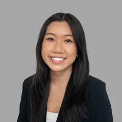 Michelle Tong smiling, with long straight dark hair, wearing a black blazer over a light top against a gray background.