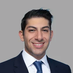 Dr. Mark Gettas is wearing a dark suit over a white collared shirt and a blue tie.