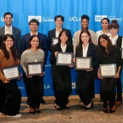 15 people smiling in front of a blue backdrop