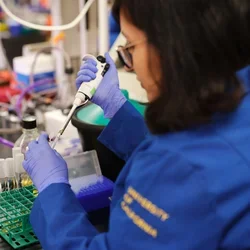 Researcher in blue lab coat using pipette 