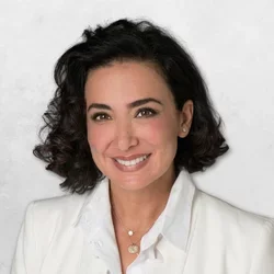 Roxana Sayah has short black hair and is wearing a white blazer and white shirt