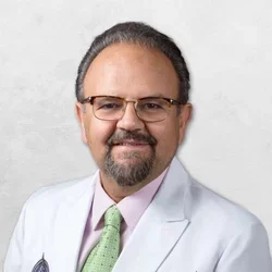 Saeid Razi is wearing glasses and a white doctor's coat over a pink shirt with a green tie