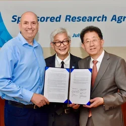 Three men smiling in front of a signed document