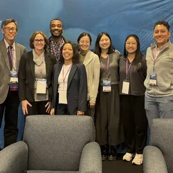 A group of eight people poses in front of a blue backdrop