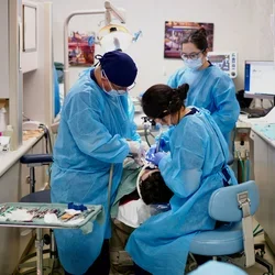 Three dentists in blue scrubs, treating a sedated patient