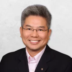William D. Nguyen is wearing a black suit with a pink shirt. He is also wearing glasses.