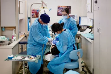 Three dentists in blue scrubs, treating a sedated patient