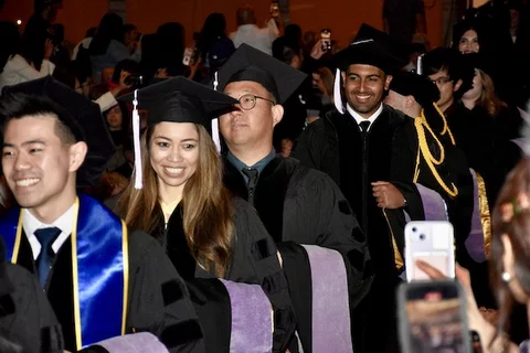 Graduates in regalia walking down an aisle