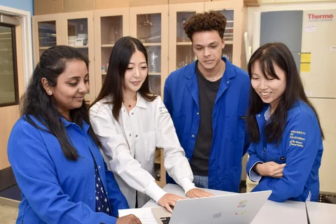 Four people in a laboratory, huddled around a laptop