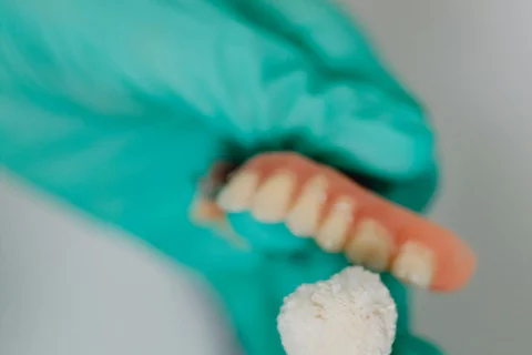 Lab technician holding dentures and using a polishing tool while wearing gloves