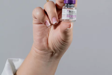 Botox vial held by a hand in a neutral setting