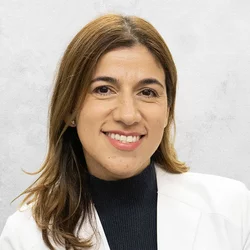 Dr. Ortega-Verdugo is wearing a black sweater and a white medical coat.