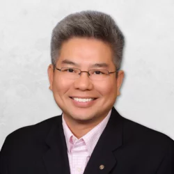 William D. Nguyen is wearing a black suit with a pink shirt. He is also wearing glasses.