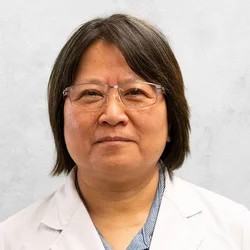 Dr. Lin is wearing a button-up shirt and a white medical coat.